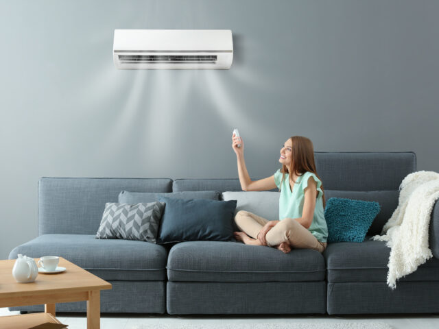 young woman on the lounge switching on the split system air conditioner with remote control